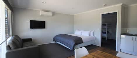 A modern hotel room with a bed, a sofa, a dining table, and a TV.