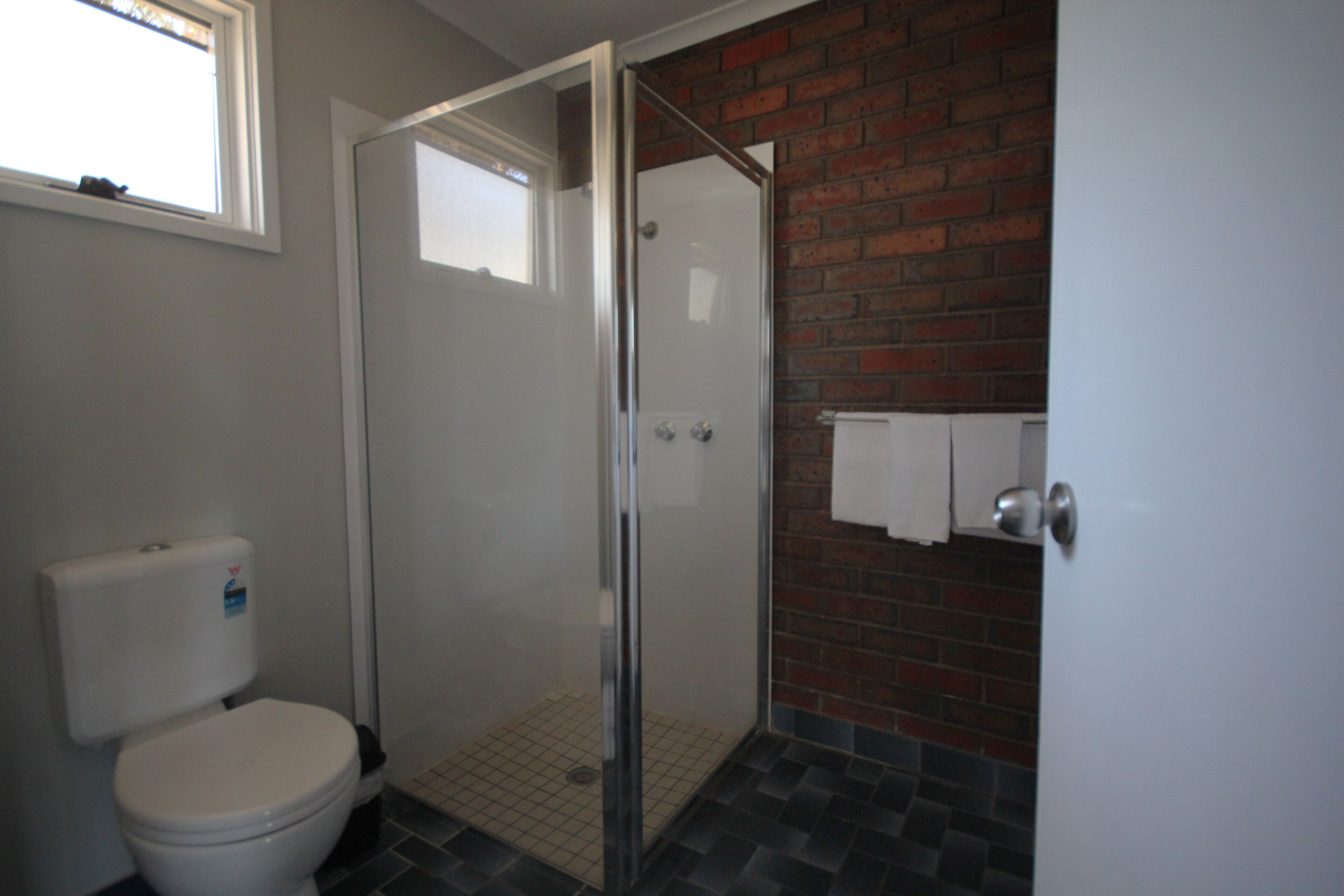 A bathroom with a toilet, a glass shower enclosure, and a brick wall.