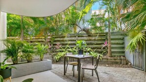 Ein Patio mit Tisch und Stühlen, umgeben von üppiger Bepflanzung und einem Holzzaun.