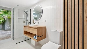 Ein modernes Badezimmer mit Duschabtrennung aus Glas, Holzwaschtisch, weißen Fliesen und einem großen Spiegel.