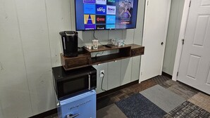 A hotel room with a flat-screen TV mounted on the wall displaying various streaming services. There is a coffee maker, a microwave, and a small refrigerator on the counter. The room has a carpeted floor and a door to the right. - Queen Bedroom In Saco (Saco)