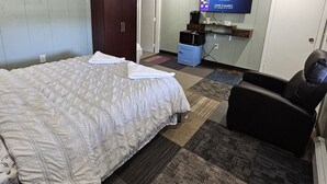 A hotel room with a large bed, a TV mounted on the wall, a desk with a computer, and a chair. - Queen Bedroom In Saco (Saco)