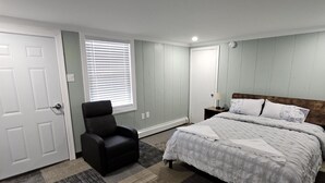 A bedroom with a bed, a chair, a window with blinds, and a door. - Queen Bedroom In Saco (Saco)
