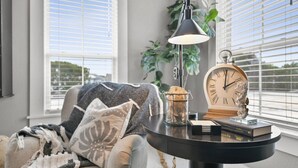 Una sala de estar acogedora con un sofá, una mesa con lámpara, un reloj y una ventana con persianas.