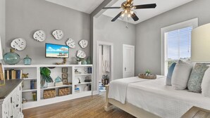 Un dormitorio con cama, televisor, ventilador de techo y ventana con persianas.