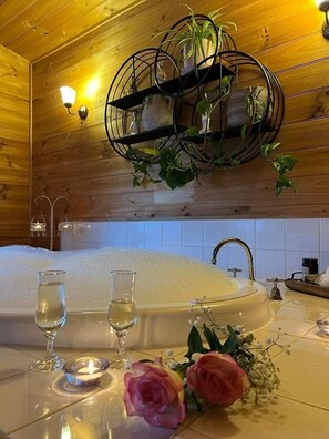A wooden interior with a bathtub, two glasses, a candle, and a rose on a table. - Murray River Spa Retreat (Echuca)