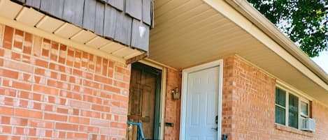 A brick building with a white door and a small window. There is a metal railing in front of the building.