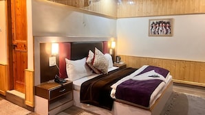 Un dormitorio con cabecera de madera, una cama con manta púrpura, una mesita de noche con lámpara y una obra de arte colgada en la pared.