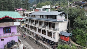 Un edificio de varios pisos con un balcón en la planta baja, un cartel que dice 'Little Italy Inn', y una casa morada contigua.