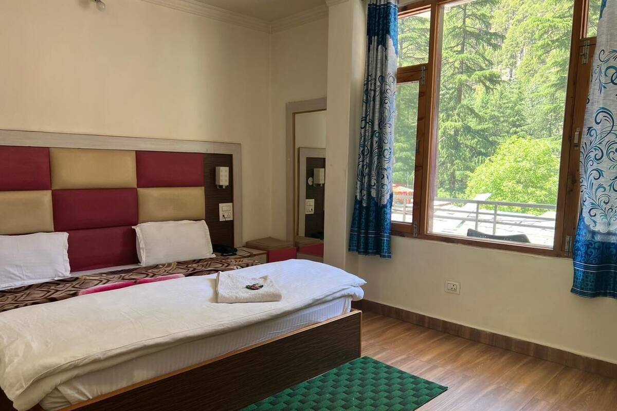 A bedroom with a bed, a headboard, a window with curtains, and a view of trees.
