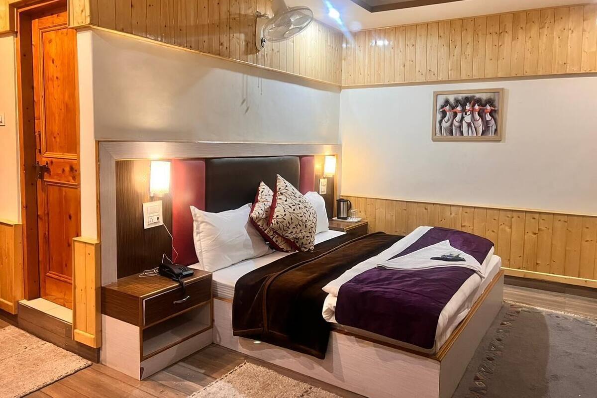 A bedroom with a bed, bedside tables, a nightstand, a wall-mounted light, a wooden door, and a framed picture on the wall.