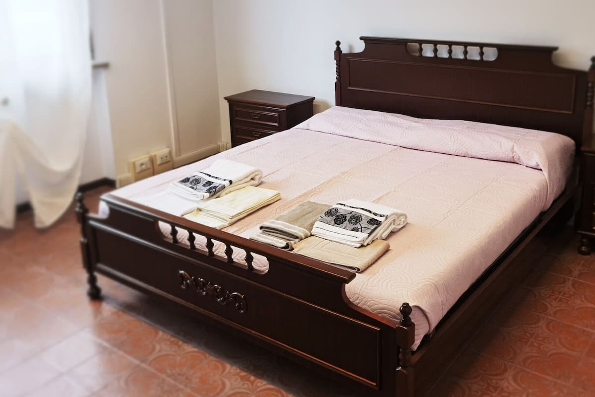 Un lit bien fait, avec une couvre-lit rose et deux serviettes pliées posées sur le pied de lit.