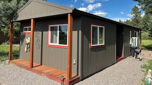A small, single-story cabin with a front porch, a red-framed window, and a door. - Dreamcatcher Bungalow 20min to W.Glacier, between Glacier&Airport (Columbia Falls)