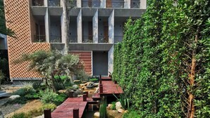 Een modern gebouw met een binnentuin, voorzien van een houten terras, een beekje en weelderige begroeiing.