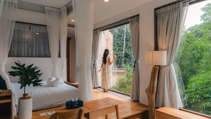Une chambre avec un lit, un bureau, une lampe et une vue sur la verdure.