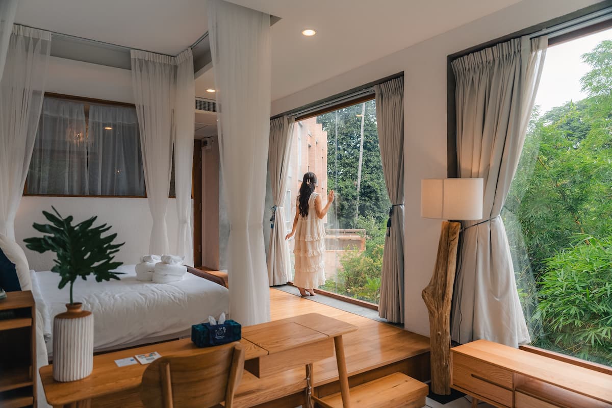 Een slaapkamer met een bed, een bureau, een lamp en uitzicht op groen.