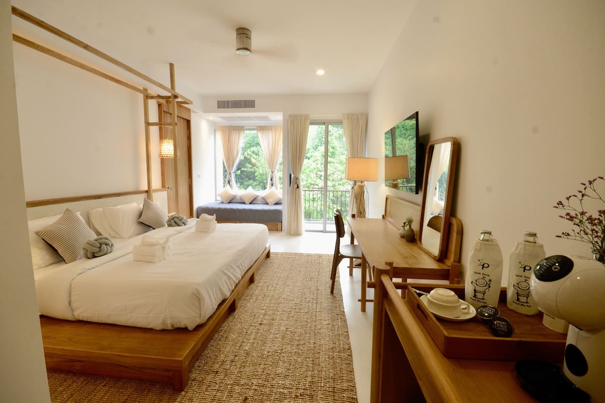 Een hotelkamer met een groot bed, een bureau met een lamp en uitzicht op groen.