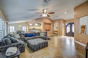 A spacious living room with a large sectional sofa, a small ottoman, and a ceiling fan.