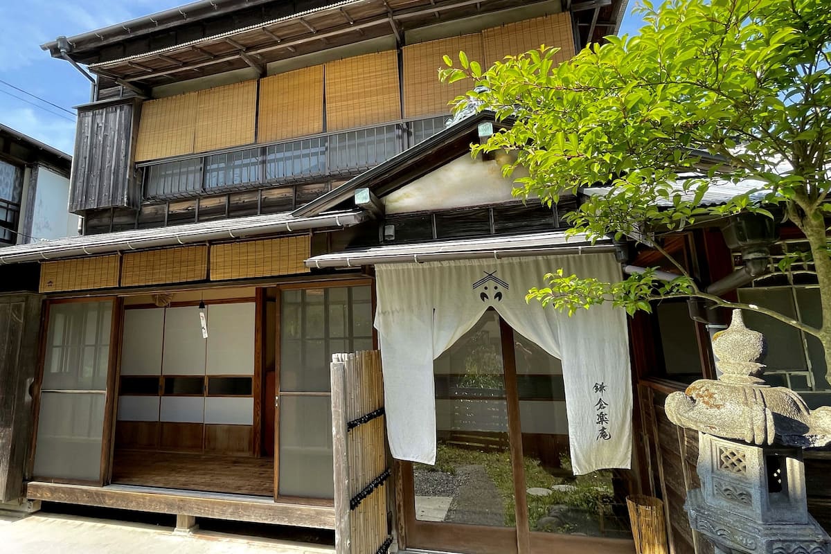 Ein traditionelles japanisches Gebäude mit Holzfassade, verschiebbaren Shoji-Türen und einem kleinen Garten, der durch die Fenster sichtbar ist.