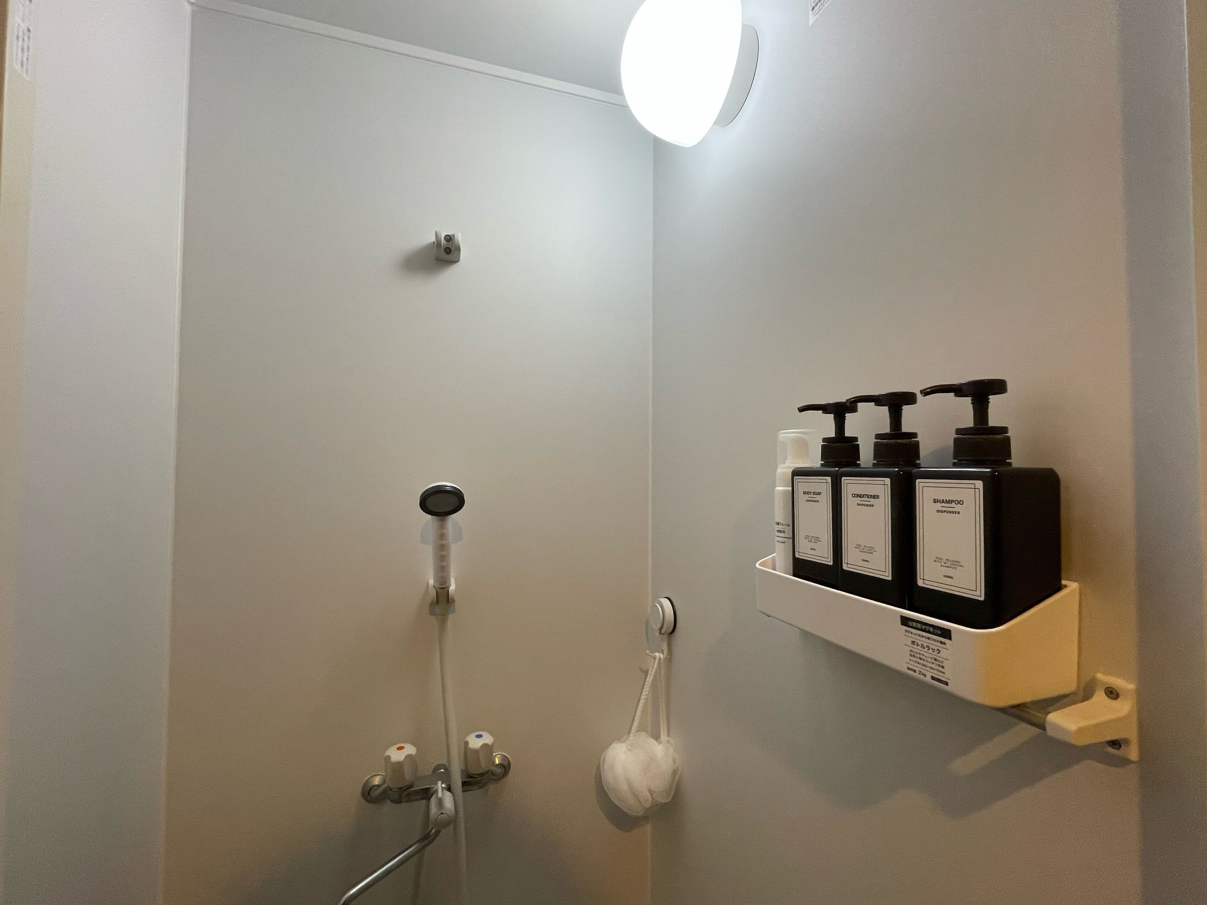 A bathroom with a shower, a hand dryer, and a shelf with toiletries.
