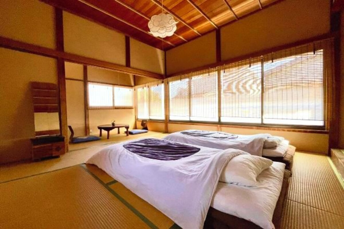 Een traditionele Japanse kamer met tatami vloerbedekking, twee bedden met wit beddengoed, een houten plafond en grote ramen met zonwering.