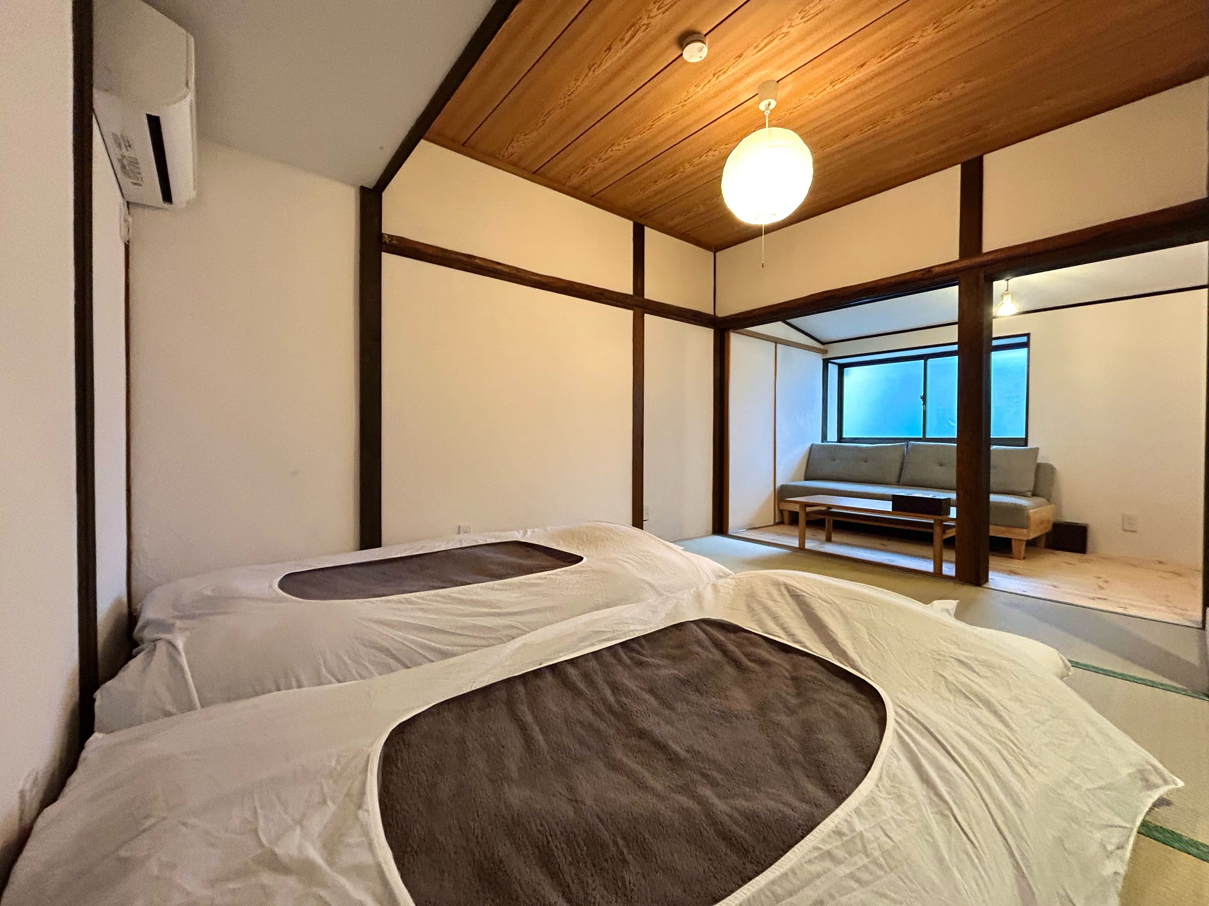 Une pièce de style japonais traditionnel, avec un sol recouvert de tatamis, un plafond bas en bois et une porte coulissante donnant sur un balcon.