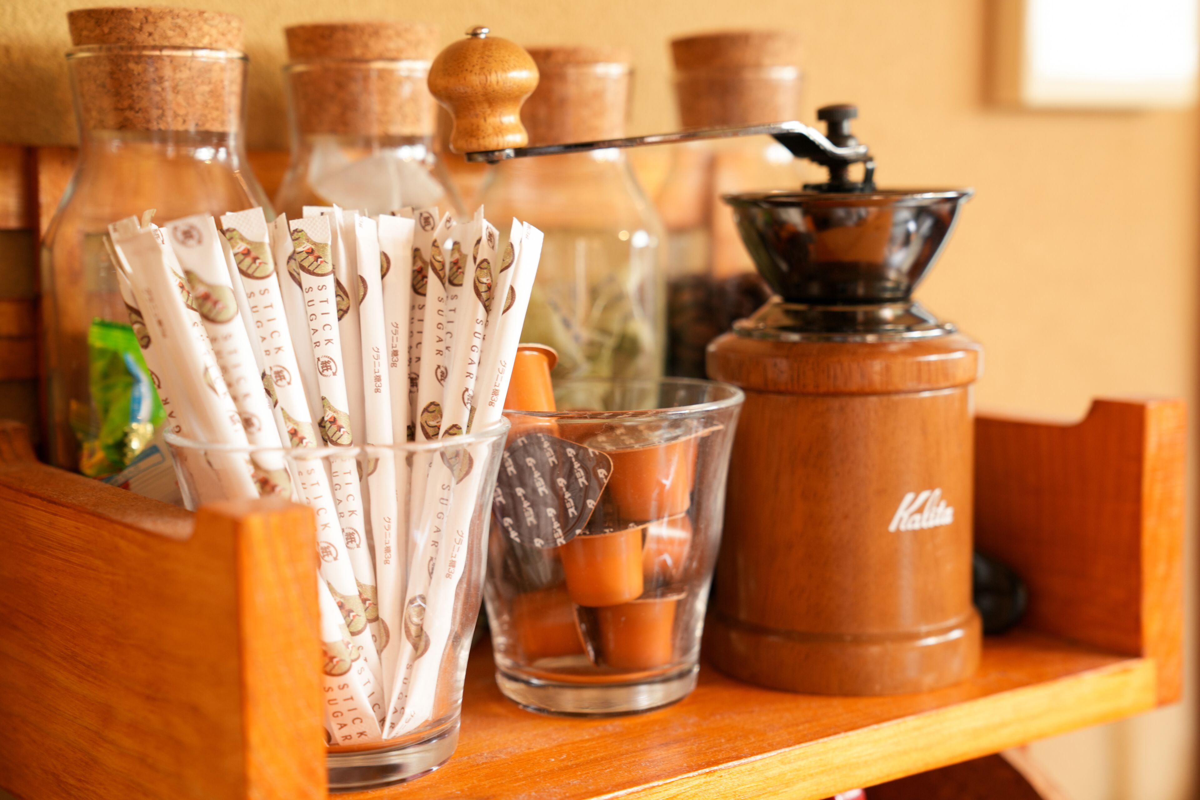 Une étagère en bois avec des bouteilles en verre, un moulin à café et des sachets de sucre.
