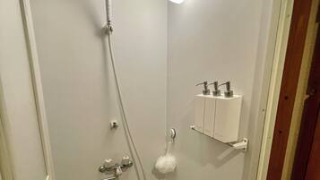 A small, enclosed shower area with a handheld showerhead, a wall-mounted light, and a soap dispenser.