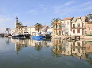 A calm harbor with boats docked, a lighthouse, and traditional buildings with palm trees.