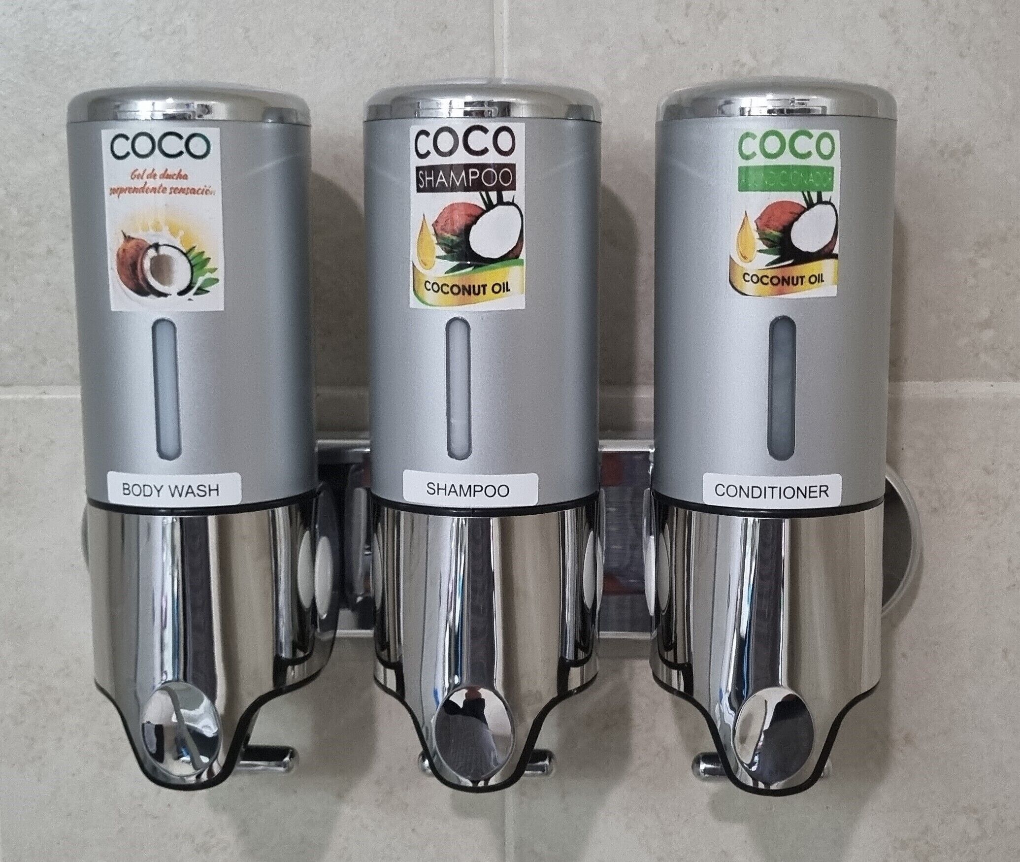 Tres dispensadores metálicos etiquetados con 'COCO' y diferentes tipos de producto: jabón corporal, champú y acondicionador.