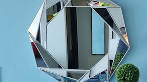 Espejo hexagonal con diseño geométrico en una pared, rodeado de decoración náutica que incluye pequeños barcos y una planta en maceta.