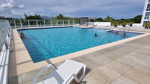 Una piscina con agua cristalina azul, rodeada por una cerca blanca y un suelo de baldosas.