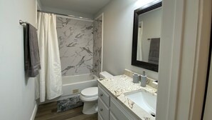 A bathroom with a bathtub, toilet, and vanity with a mirror.