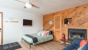 Una habitación con cama, sofá, televisor, chimenea y ventilador de techo.