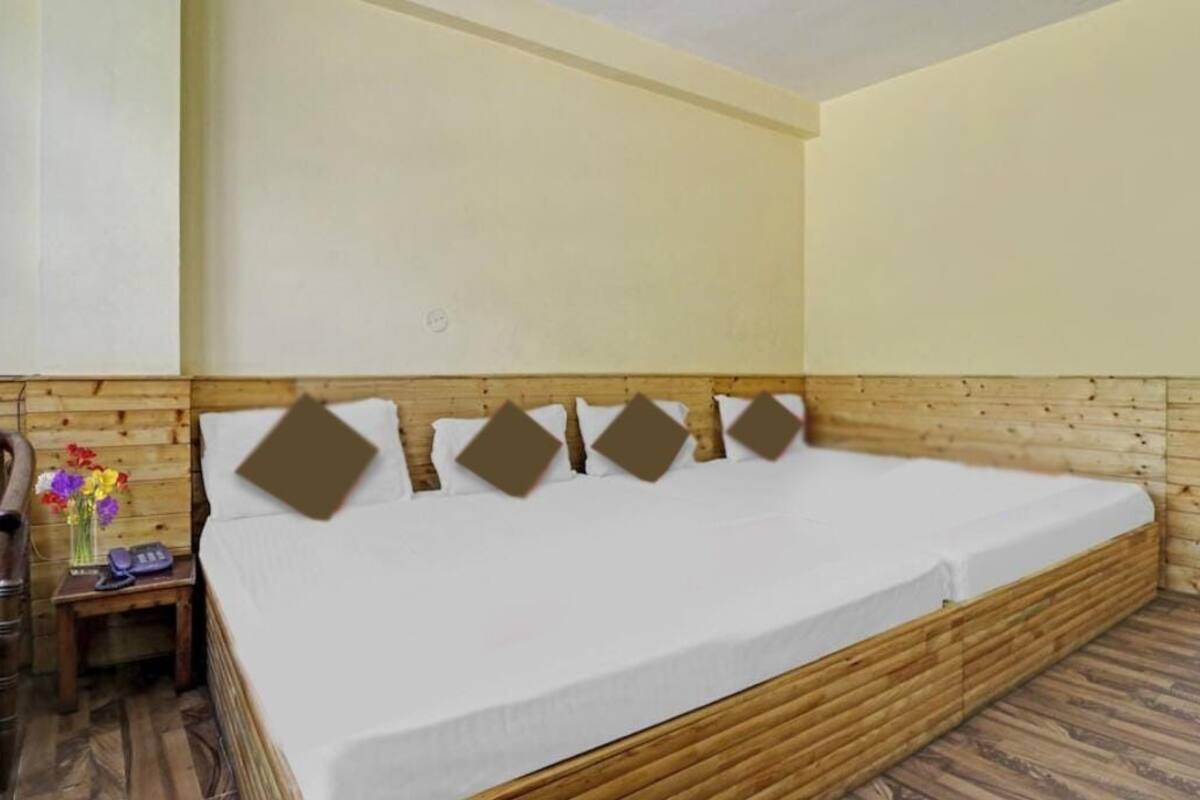 A room with a wooden headboard, a bed with a white mattress, and a small bedside table with a vase of flowers.