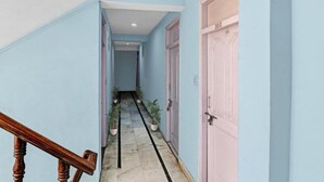 A hallway with light blue walls, a marble floor, and wooden railings. There are potted plants along the wall and a door with the number 203 visible. - Hotel Beas Valley (Manali)
