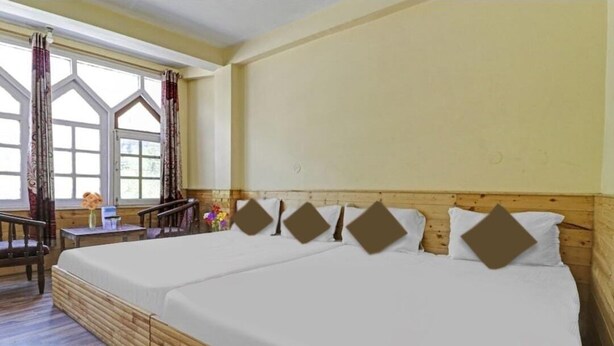 A room with two beds, a wooden floor, a window with curtains, and a small table with a vase. - Hotel Beas Valley (Manali)
