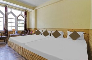 Ein Zimmer mit zwei Betten, Holzboden, einem Fenster mit Vorhängen und einem kleinen Tisch mit einer Vase.
