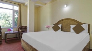 A hotel room with a large bed, a small table with a vase of flowers, a chair, and a window with curtains. - Hotel Beas Valley (Manali)