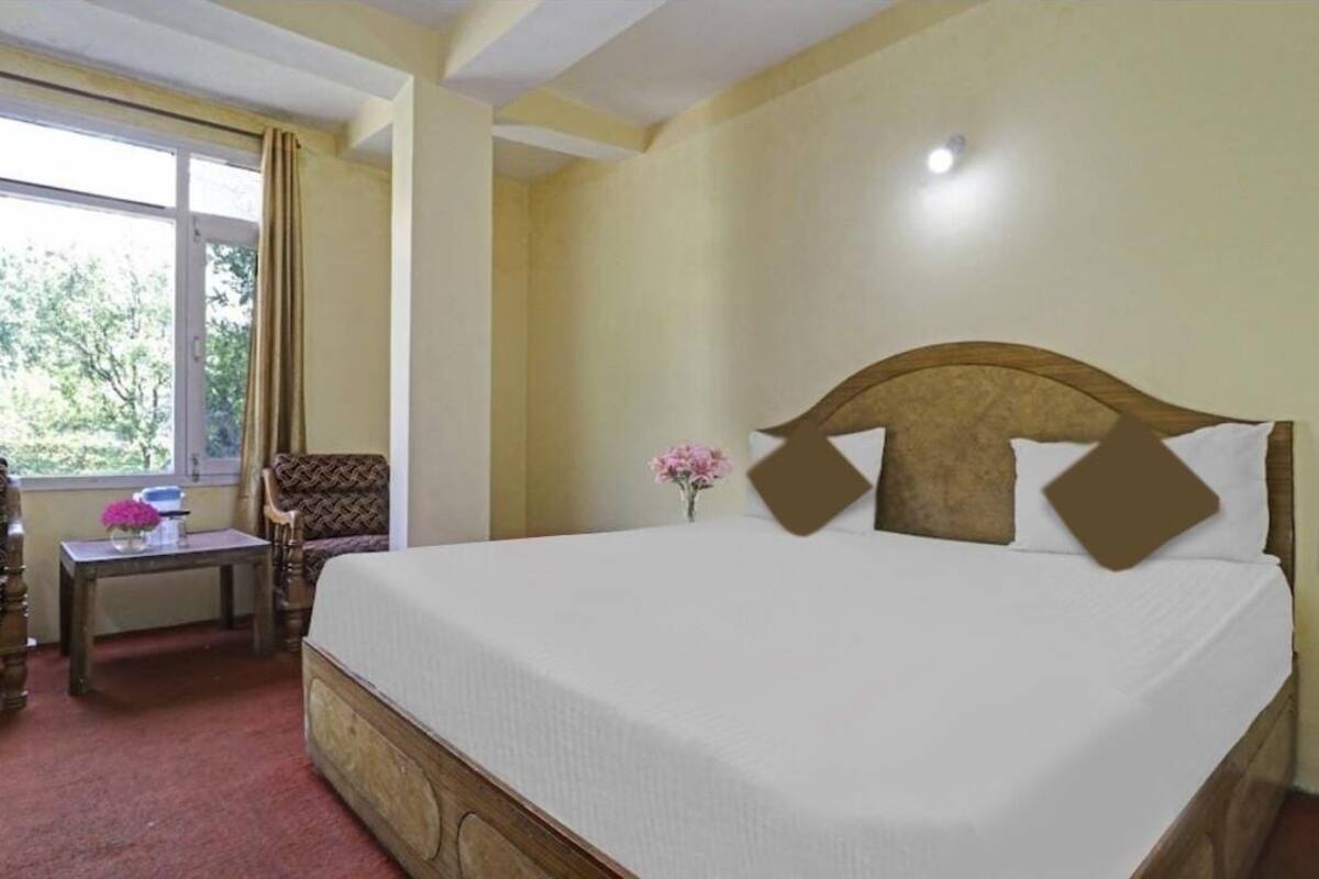 A hotel room with a large bed, a small table with a vase of flowers, a chair, and a window with curtains.
