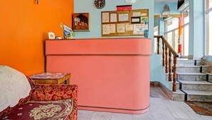 A reception area with a pink counter, a bulletin board with notices, a clock, and a staircase leading upstairs. - Hotel Beas Valley (Manali)
