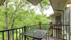 Un espace extérieur abrité, doté d’une table et de chaises en métal, entouré d’une terrasse en bois et d’une rambarde en métal, et offrant une vue sur un paysage verdoyant luxuriant.