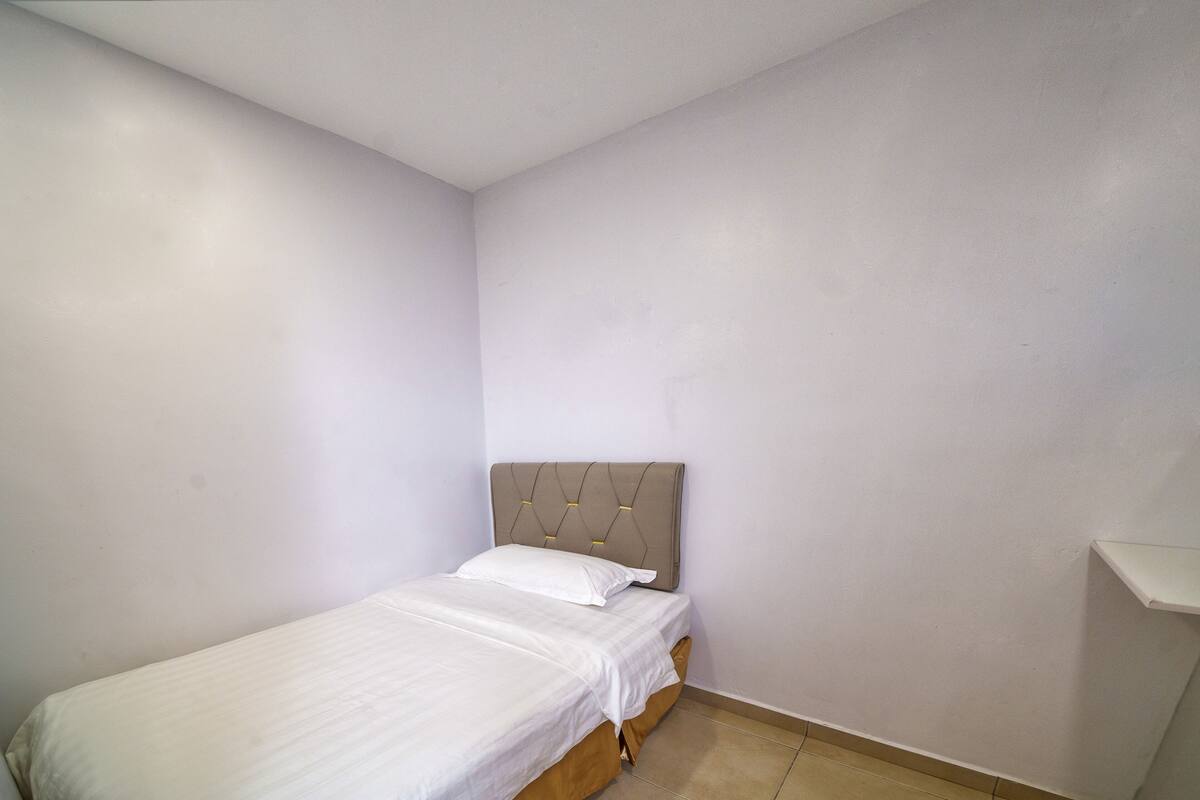 Ein kleines Zimmer mit einem Einzelbett, einem schlichten Kopfteil und einer weißen Bettdecke.