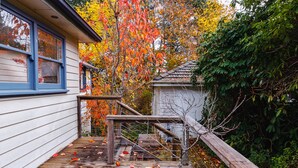 A wooden deck with a metal fence, a house with blue-framed windows, and autumn foliage.