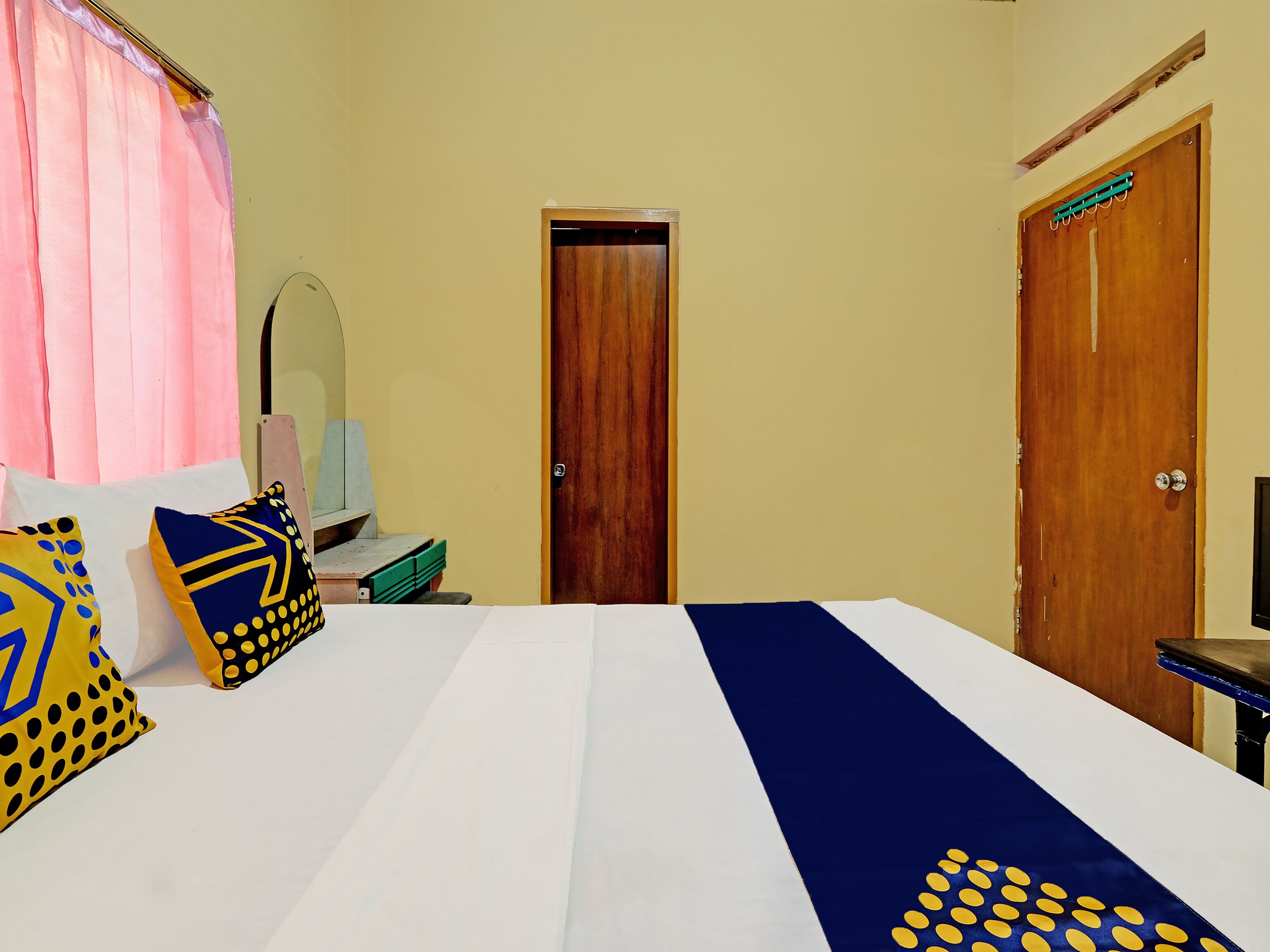 A bedroom with a bed, pillows, a mirror, and two doors.