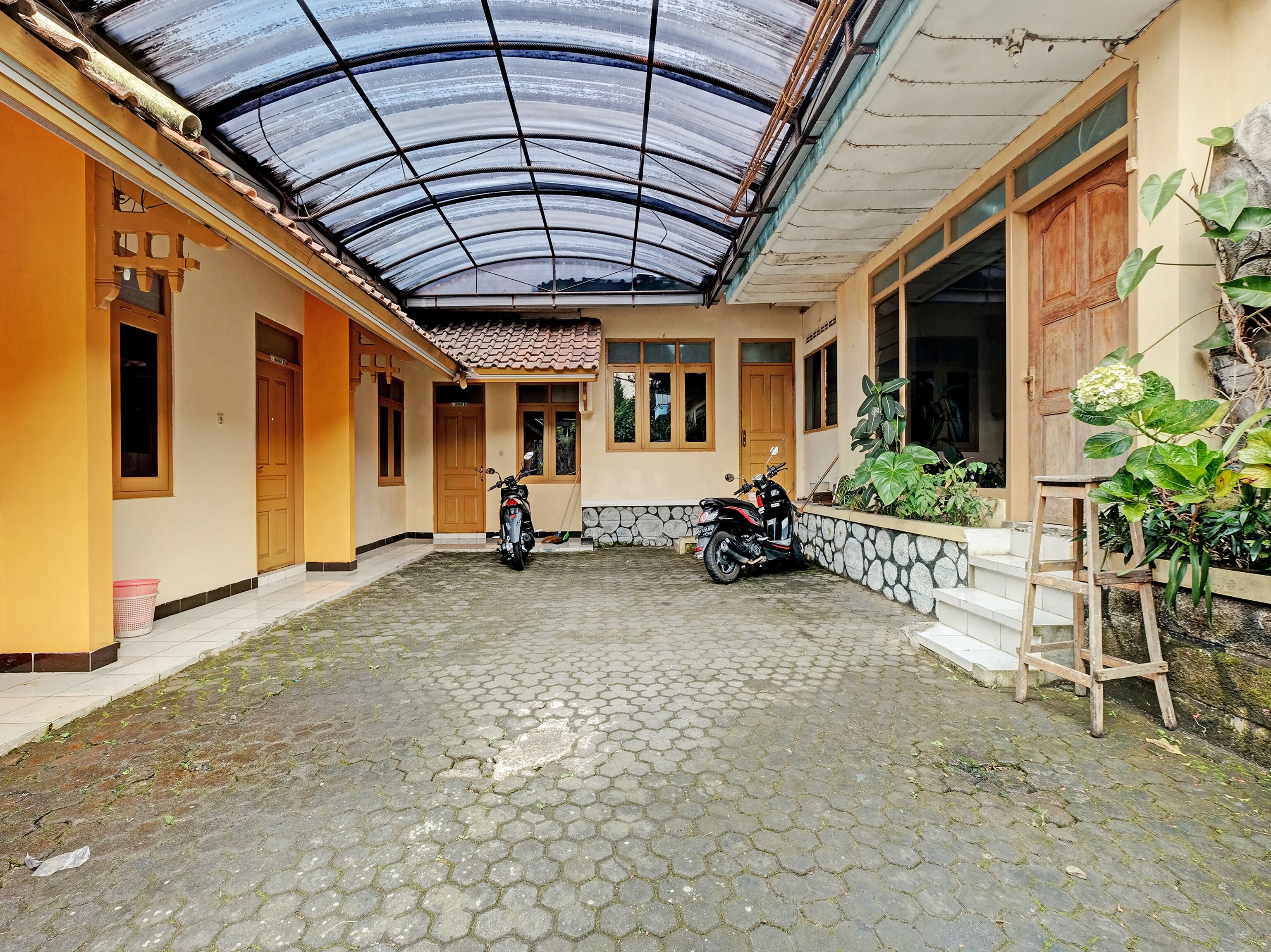 A covered courtyard with a scooter parked in the center, surrounded by a stone wall and potted plants.