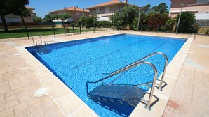 Una piscina rectangular con una escalera metálica y escalones, rodeada por un suelo de baldosas y una valla.