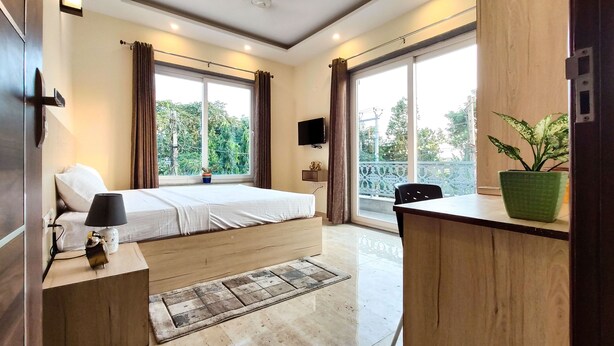 A modern bedroom with a bed, bedside table, lamp, TV, and a potted plant. - Covie Gurgaon 42 (Gurugram)