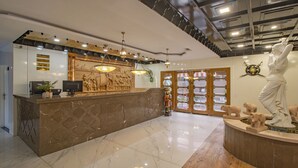 Zona de recepción con mostrador de mármol, una mesa de recepción, una estatua y un relieve decorativo en la pared.