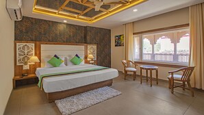 Una habitación de hotel con una cama grande, dos lámparas de noche, un cabecero de madera, un panel decorativo en la pared, una ventana con vistas y una pequeña mesa con dos sillas.